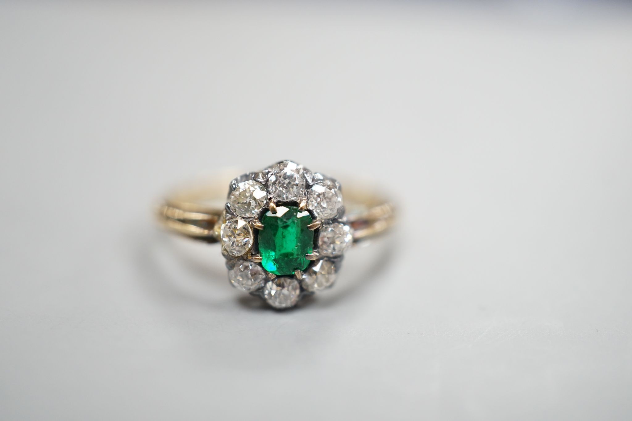 A yellow metal, emerald and diamond set oval cluster ring, size M/N, gross weight 3.1 grams.